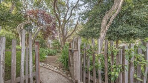 Une porte en bois mène à un chemin de gravier bordé d’une végétation luxuriante et d’arbres.