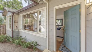 Une maison avec un porche couvert, une porte bleue et un intérieur visible, avec un canapé et des coussins.