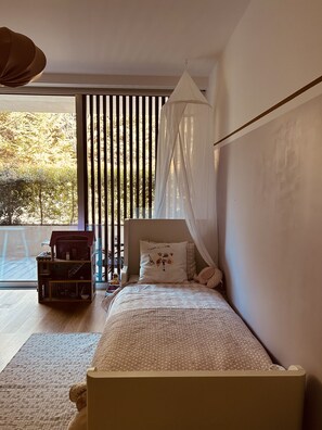 Une chambre à coucher avec un lit, une fenêtre avec des stores, une petite table et une maison de jeu.
