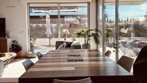 Et moderne spiseområde med et stort træbord, flere stole og udsigt til bylandskab gennem store vinduer.