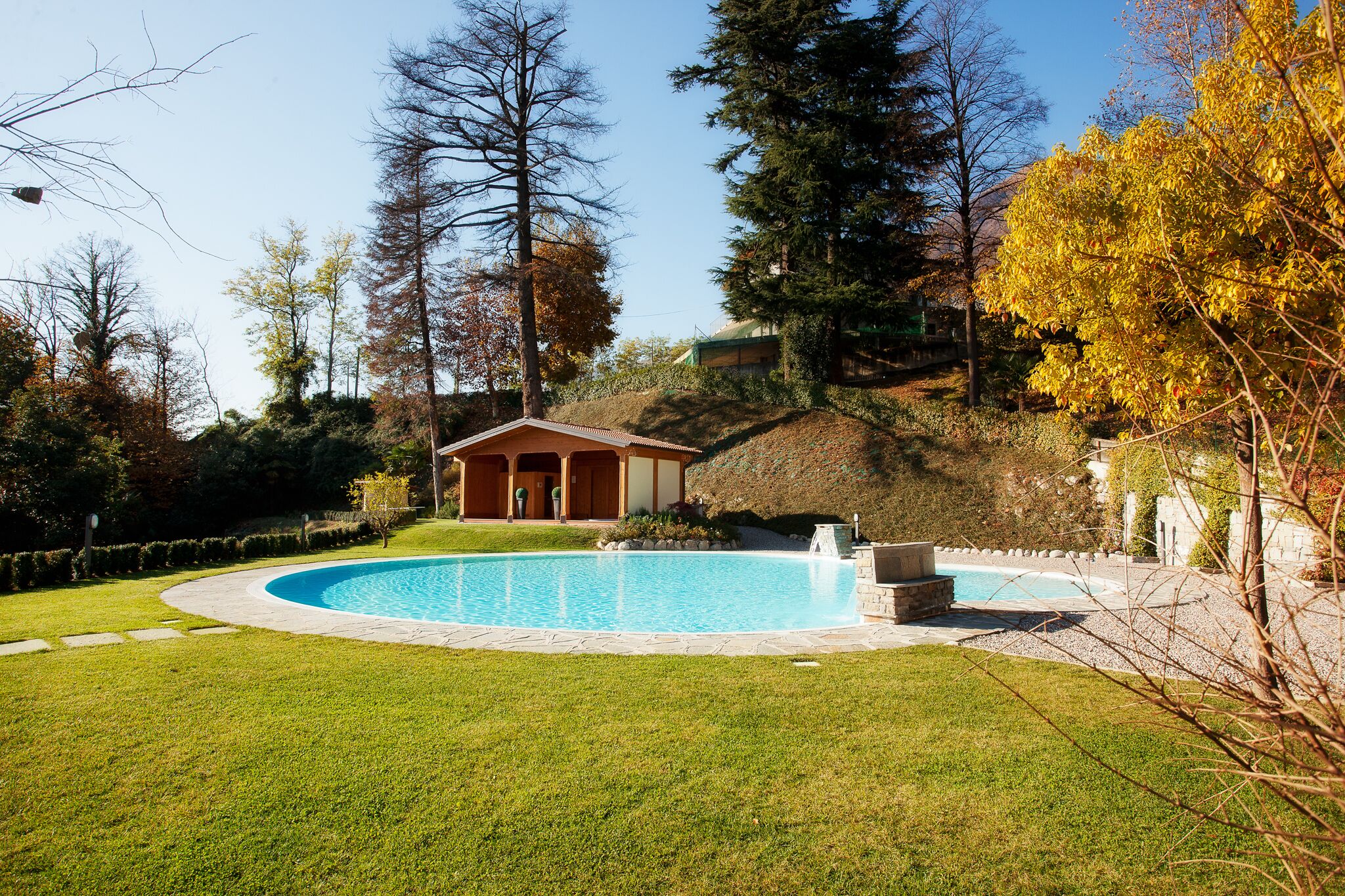 Une piscine dotée d’une terrasse en bois, entourée d’une pelouse bien entretenue et d’arbres.