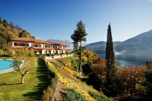 Un grand bâtiment à deux étages, doté d’un toit recouvert de tuiles rouges, situé sur une colline et offrant une vue sur un lac et des montagnes en arrière-plan.