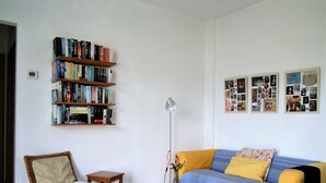 A living room with a bookshelf, a chair, a small table, a sofa, and a wall with photos. - 3-room House With Sea View (Ierapetra)