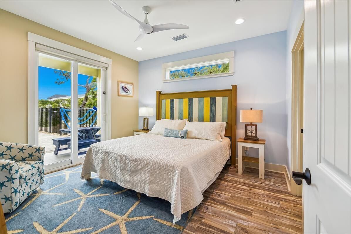 A bedroom with a bed, a nightstand, a chair, a ceiling fan, and a view of the outside.