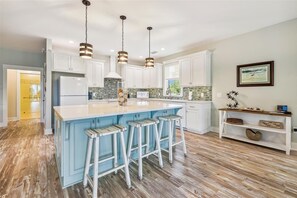 A modern kitchen with white cabinets, a large island with bar stools, and pendant lighting.