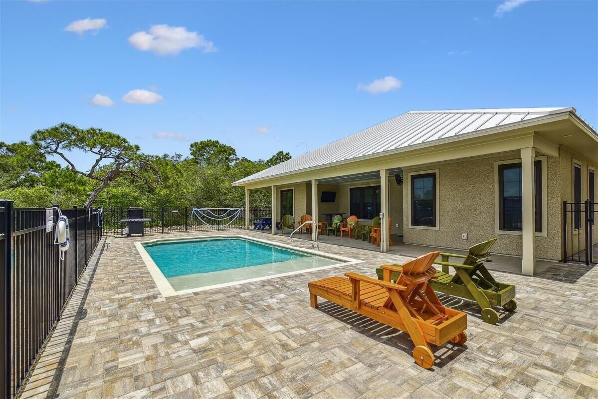Zona de piscina con terraza de baldosas, sillas de descanso y un porche cubierto con mobiliario de exterior.