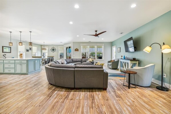 A spacious living room with a large L-shaped sectional sofa, a dining area with a table and chairs, and a kitchen area with a bar.