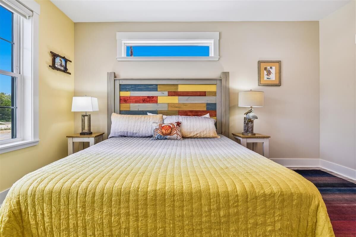 A hotel room with a large bed, a window, a bedside table with a lamp, and a wall-mounted artwork.