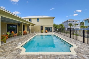 A swimming pool with a tiled deck, surrounded by colorful chairs and a covered area with a roof.