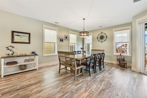 A dining area with a wooden table and chairs, a hanging light fixture, and a wall-mounted clock.