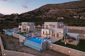 A modern villa with a swimming pool, outdoor seating, and a view of the surrounding landscape.