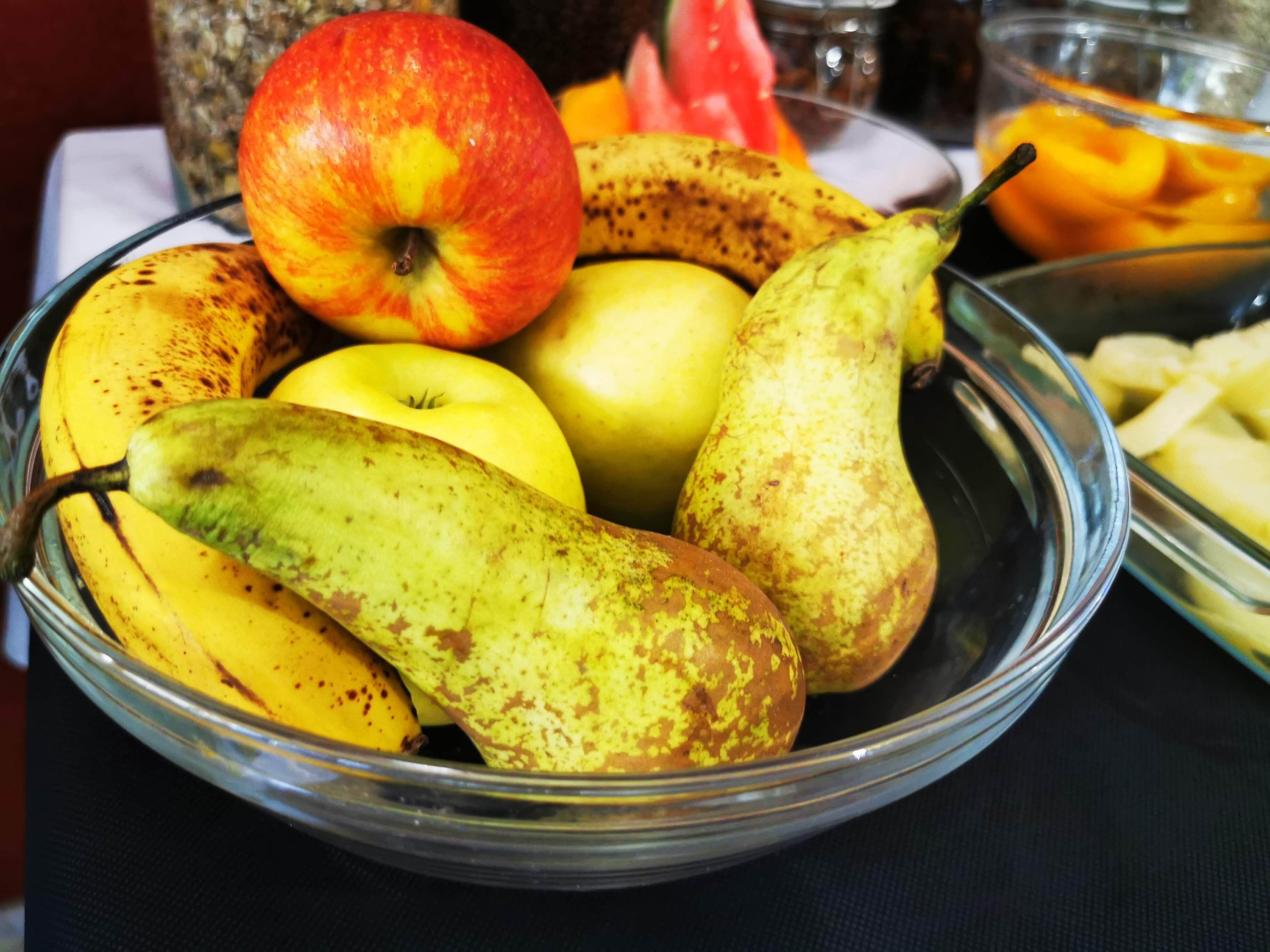 Un bol con varias frutas, incluyendo plátanos, manzanas y peras.