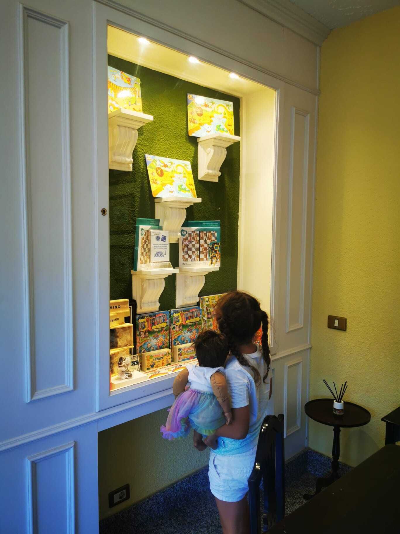 Un enfant et un adulte regardent une sélection de livres pour enfants exposés dans une pièce aux murs verts, où se trouve une petite table.