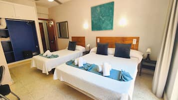 Habitación de hotel con dos camas, un ventilador de techo, un cuadro en la pared y una mesita con toallas.