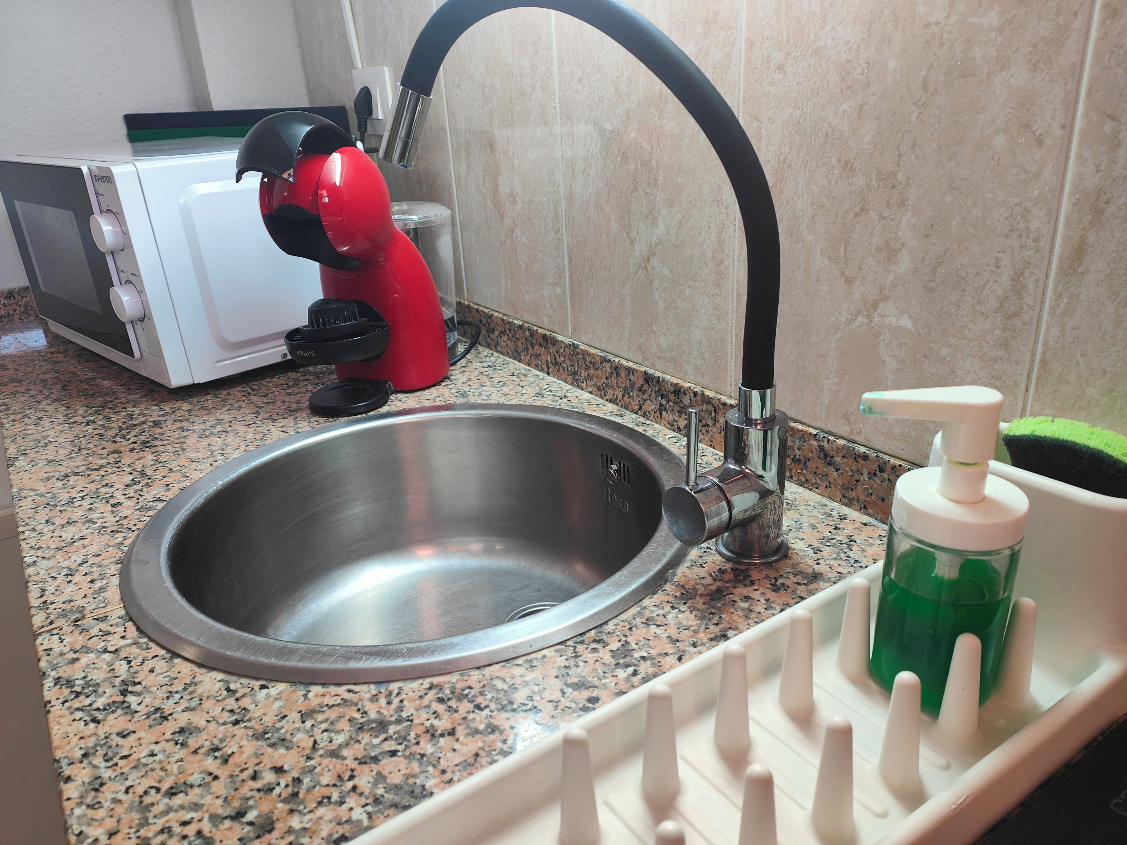 A stainless steel sink with a modern faucet, a red coffee maker, a white microwave, and a soap dispenser on the countertop.