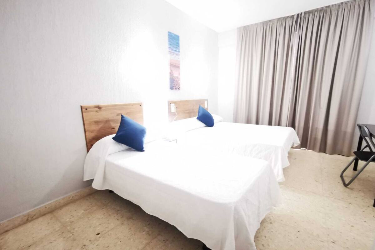 Una habitación de hotel con dos camas individuales, un cabecero de madera, una mesita y una cortina.