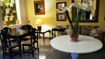 A hotel lobby with a round table, chairs, a sofa, a lamp, and framed pictures on the wall.