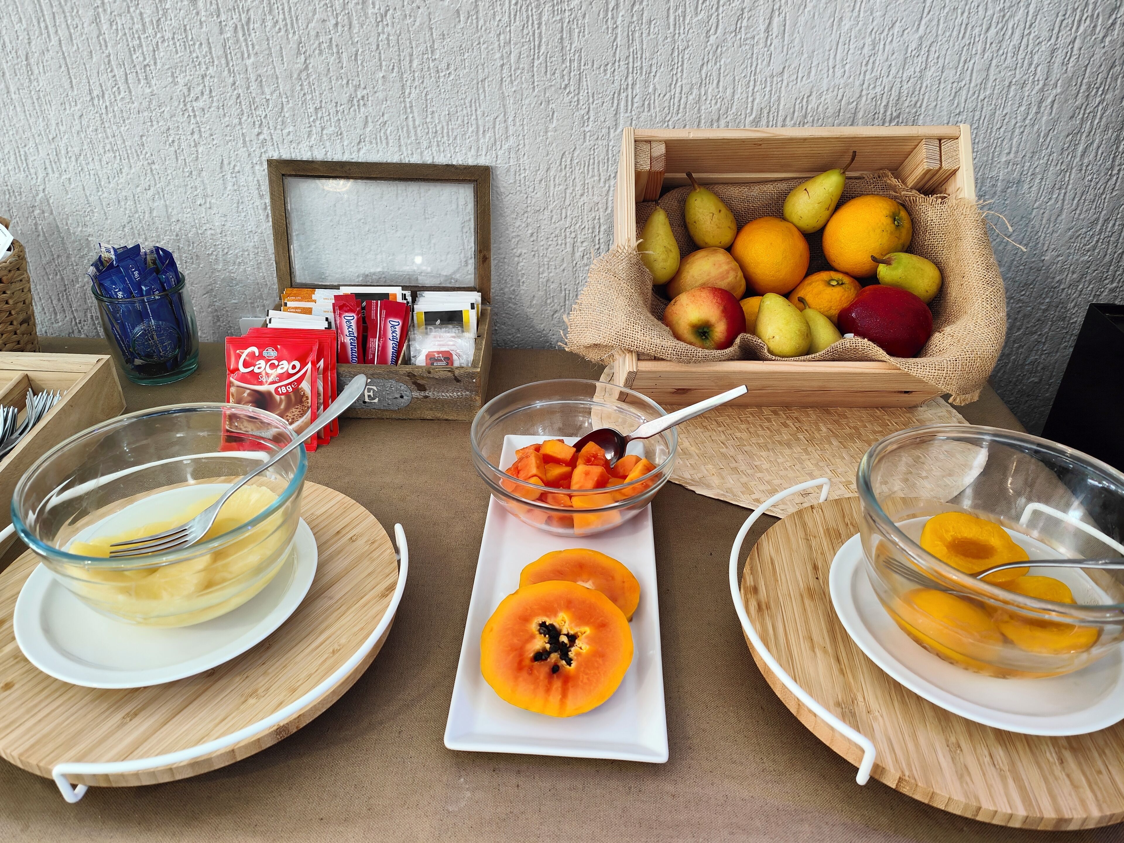 Une table dressée pour le petit-déjeuner, avec des bols de fruits, un panier de fruits et des en-cas emballés.