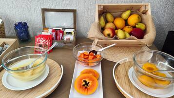Une table dressée pour le petit-déjeuner, avec des bols de fruits, un panier de fruits et des en-cas emballés.