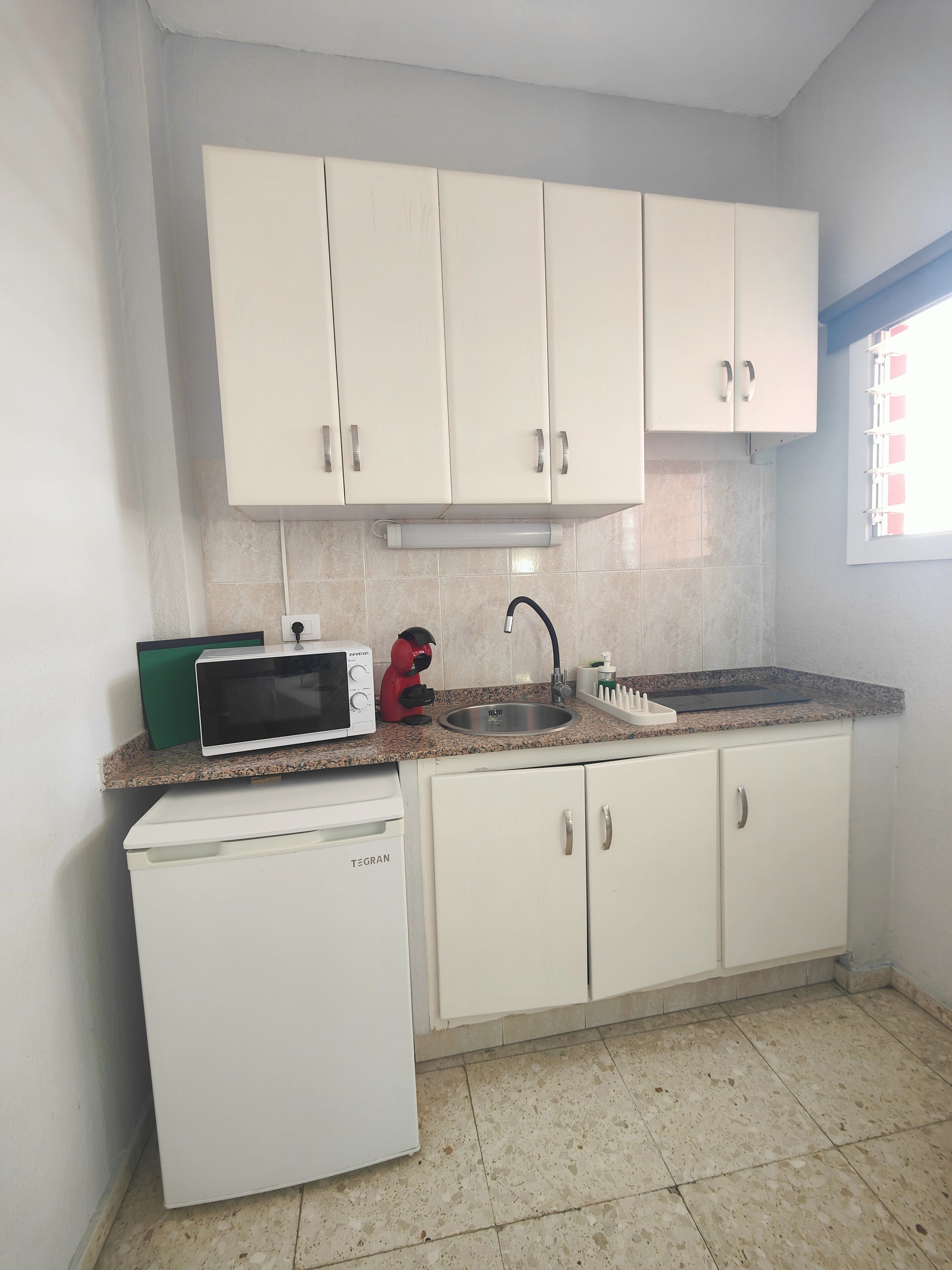 A compact kitchen with white cabinets, a built-in microwave, a small refrigerator, and a sink with a faucet.
