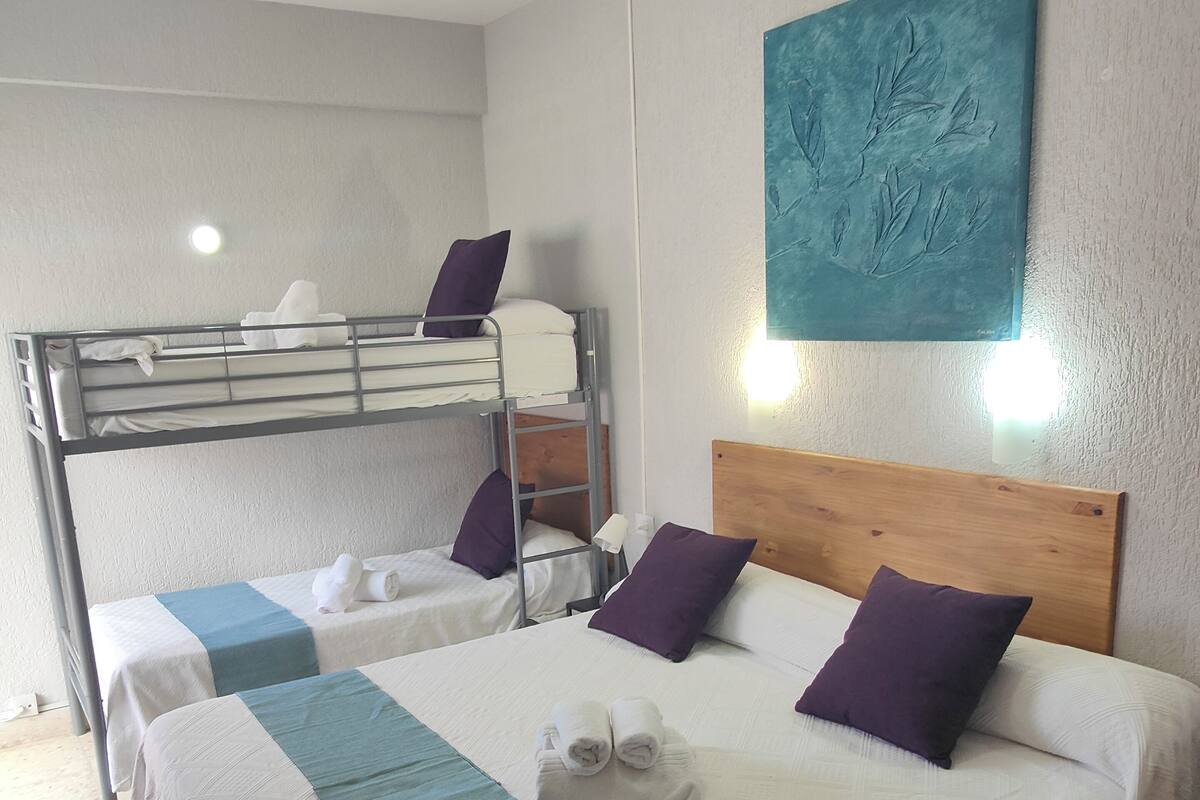 Habitación de hotel con literas, una cama individual con cabecera de madera y un ventilador de techo.
