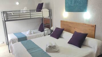 Une chambre d’hôtel avec un lit superposé, un lit simple doté d’une tête de lit en bois et un ventilateur de plafond.