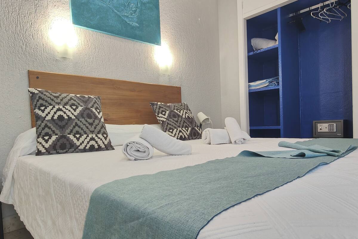 Una cama bien hecha con almohadas estampadas, una toalla enrollada y una manta color turquesa.