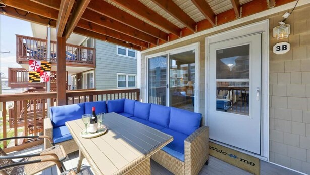 Un espace extérieur aménagé, abrité et doté d'un canapé et d'une table en osier, d'une terrasse en bois et d'une porte-fenêtre coulissante donnant accès à une pièce.