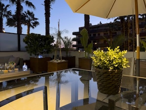 A glass-top table with a potted plant, outdoor seating, and palm trees.
