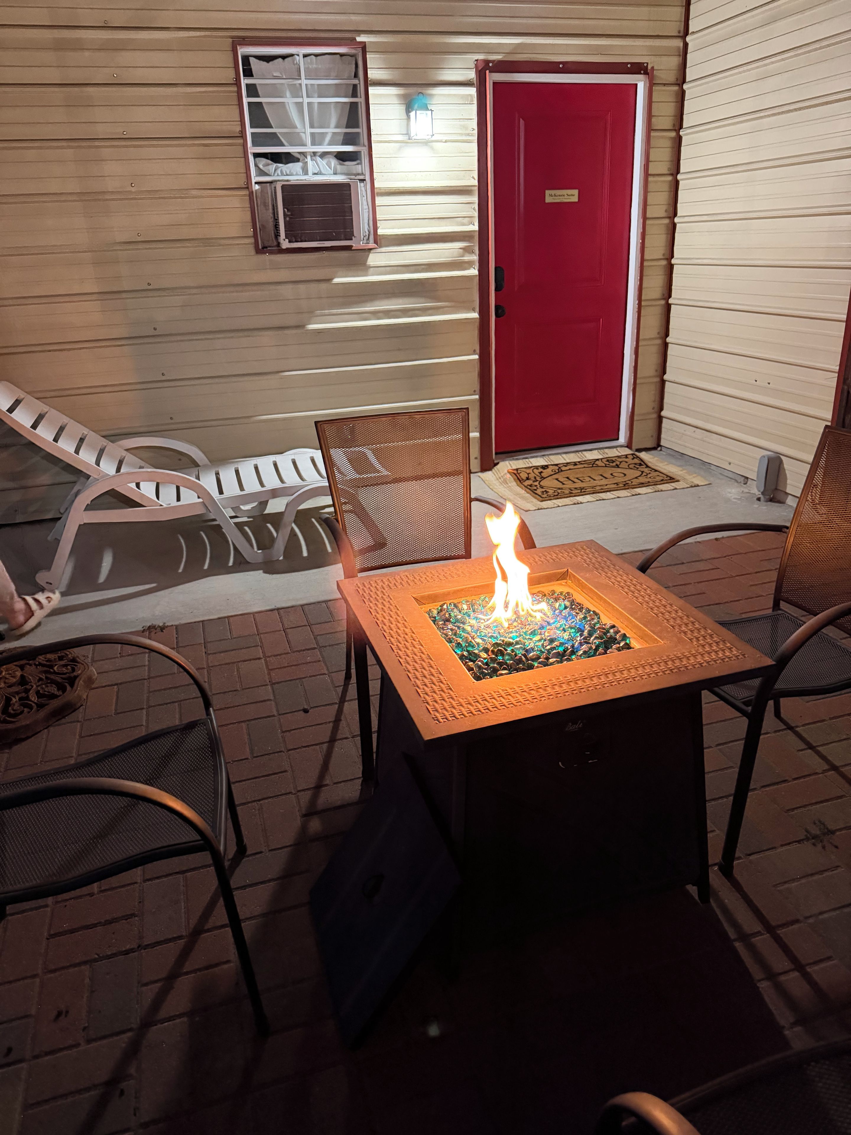 An outdoor seating area with a fire feature, a red door, and a window with curtains.
