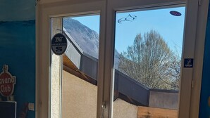 Una habitación con un gran ventanal que da al exterior, suelo de madera, una silla de mimbre y una lámpara en el techo.