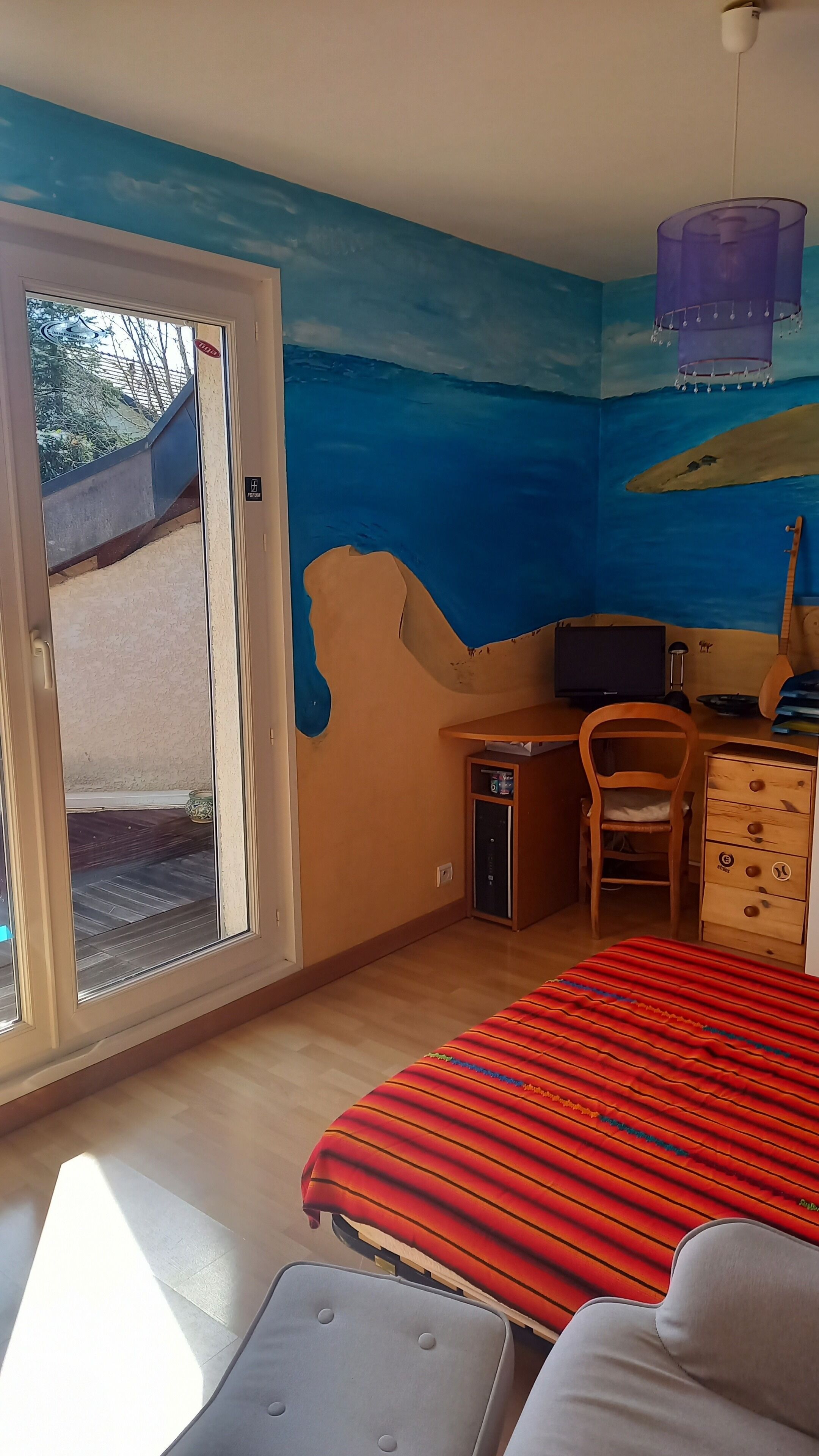 Une pièce comprenant un lit, un bureau, une chaise, une commode et une porte-fenêtre coulissante donnant sur un espace extérieur.