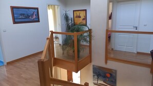 Una habitación con una escalera de madera, una planta en maceta y dos cuadros en las paredes.
