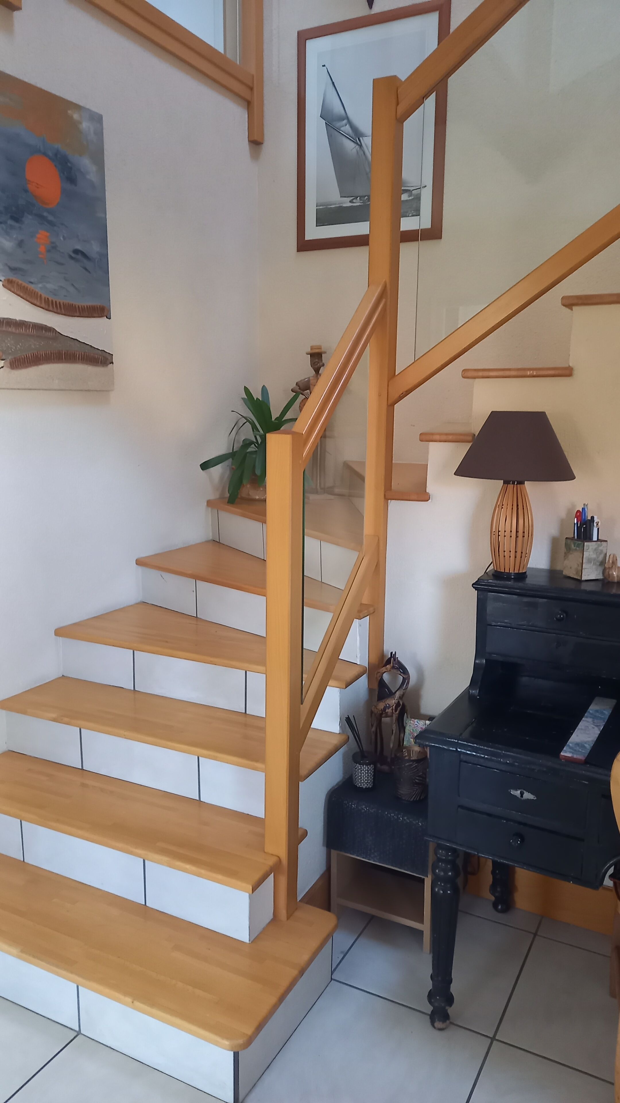 Una escalera de madera con peldaños y barandilla, que conduce a un rellano con un piano y una lámpara.