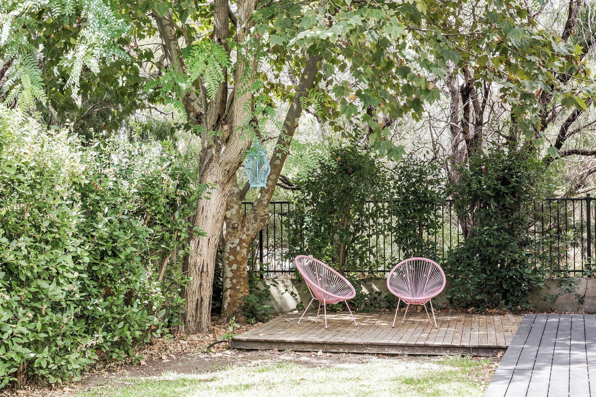 Een houten terras met twee roze stoelen en een vogelhuis.