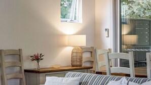 A cozy room with a bed, a bedside table with a lamp, a vase with flowers, and a window with blinds.