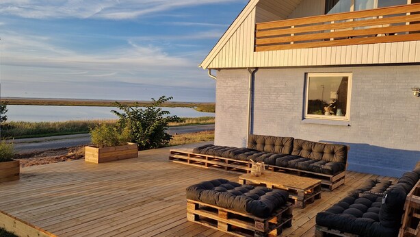 A modern house with a deck featuring outdoor seating and a view of a lake. - Large holiday house with great seaview - sauna and hottub (Glesborg, Bønnerup Strand)