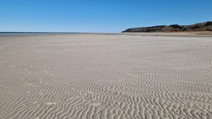 A wide sandy beach with gentle waves, a clear sky, and a distant hill with sparse vegetation. - Large holiday house with great seaview - sauna and hottub (Glesborg, Bønnerup Strand)