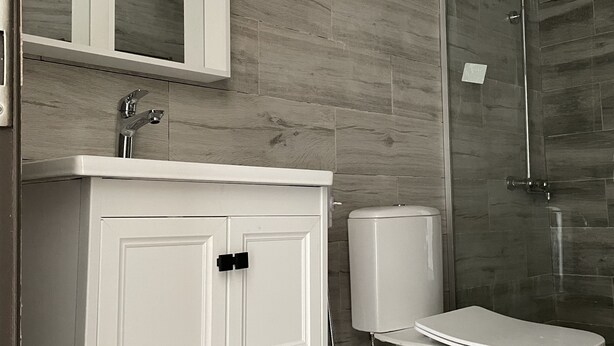 Un baño moderno con un tocador blanco, una cabina de ducha de vidrio y un inodoro.