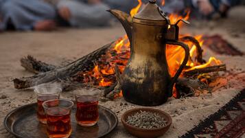Una disposición tradicional para el té, con un hervidor metálico, tres vasos de té y un cuenco de hierbas sobre una bandeja, con un fuego como fondo.