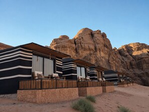 A row of modern, striped-roofed cabins with outdoor seating, set against a backdrop of rocky cliffs.