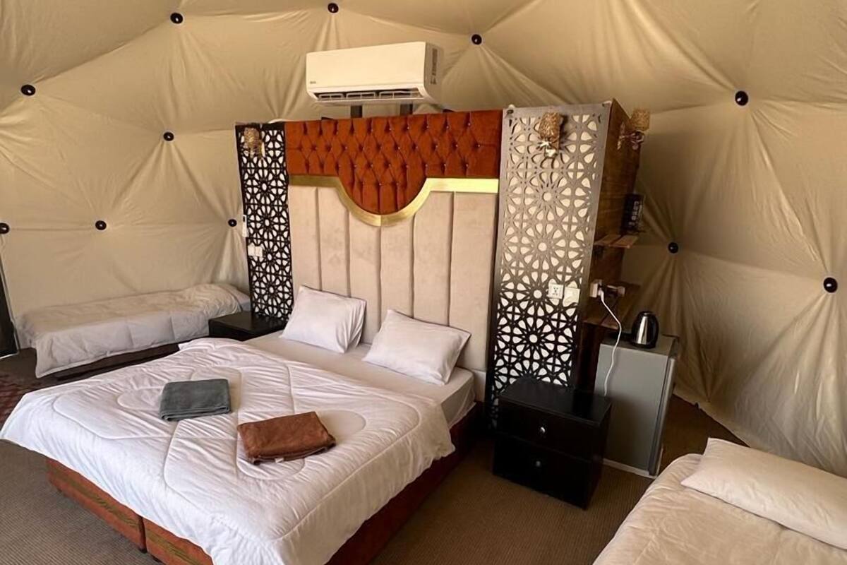 A tent-style room with two beds, a decorative headboard, and a small table with a lamp.