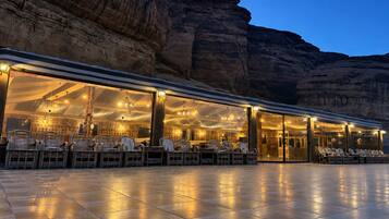 An outdoor dining area with chairs and tables, set against a rocky cliff backdrop.