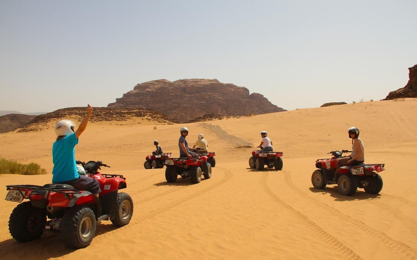 A group of people on quad bikes in a desert landscape with sand dunes and rocky formations.