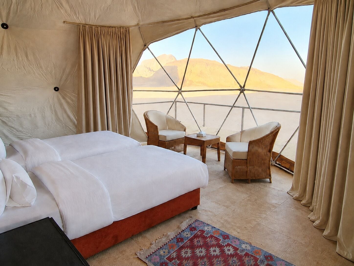Een tent met een bed, twee stoelen, een klein tafeltje en uitzicht op de woestijn.