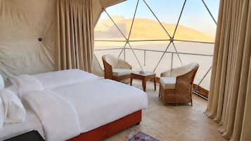 Una habitación con tienda de campaña, una cama, dos sillas, una mesita y vista al desierto.