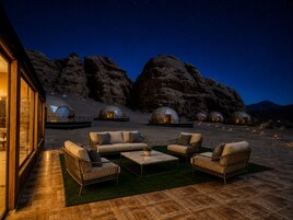 Un resort en el desierto con varias cabañas en forma de cúpula, mobiliario exterior y vistas a montañas rocosas al anochecer.