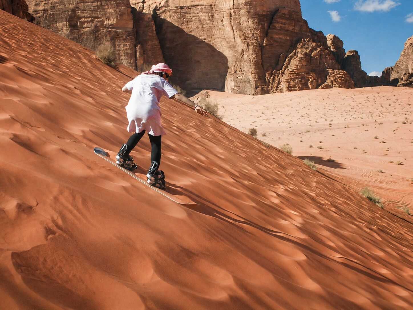 A person snowboarding down a sandy slope with rock formations in the background.