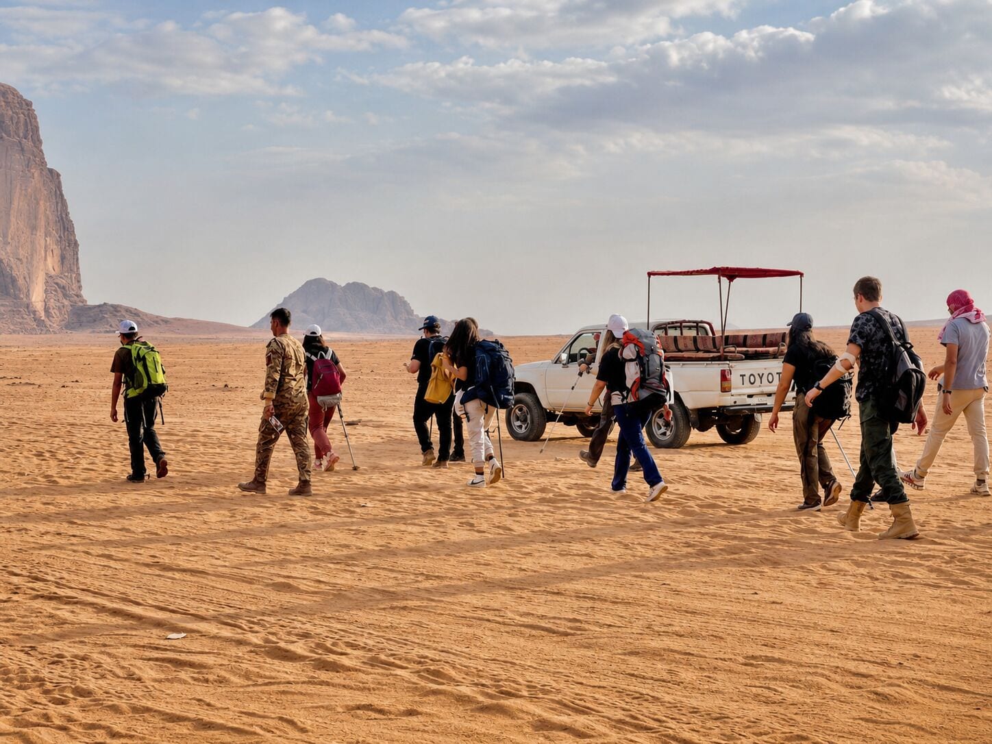 A group of people walking in a desert with a pickup truck.