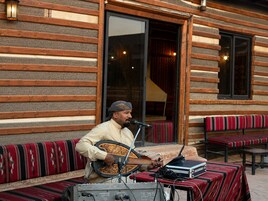 Una persona tocando un instrumento de cuerda al aire libre, con un micrófono y equipo electrónico sobre una mesa.